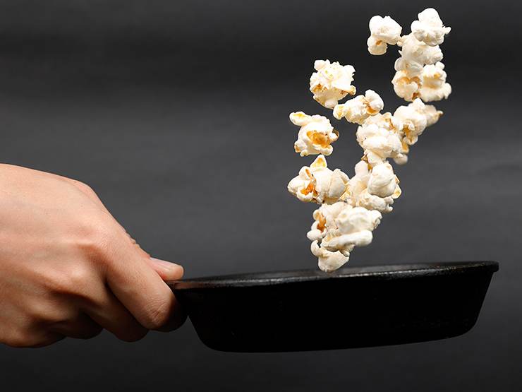 Human hand tossing popcorn on a pan to make homemade popcorn