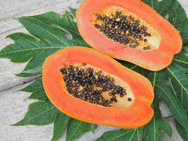 Two slices of ripe papayas with seeds and leaves